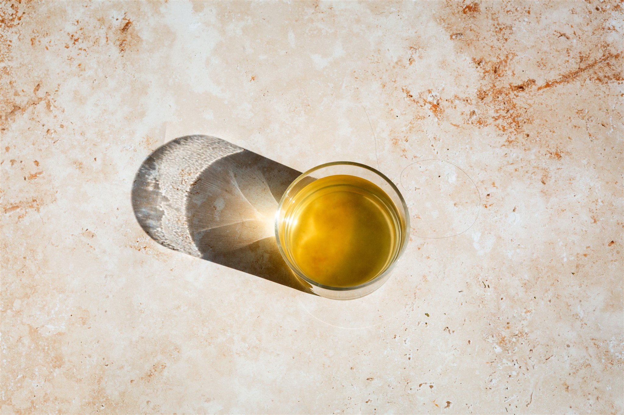 Glass of yellow liquid on a textured beige surface
