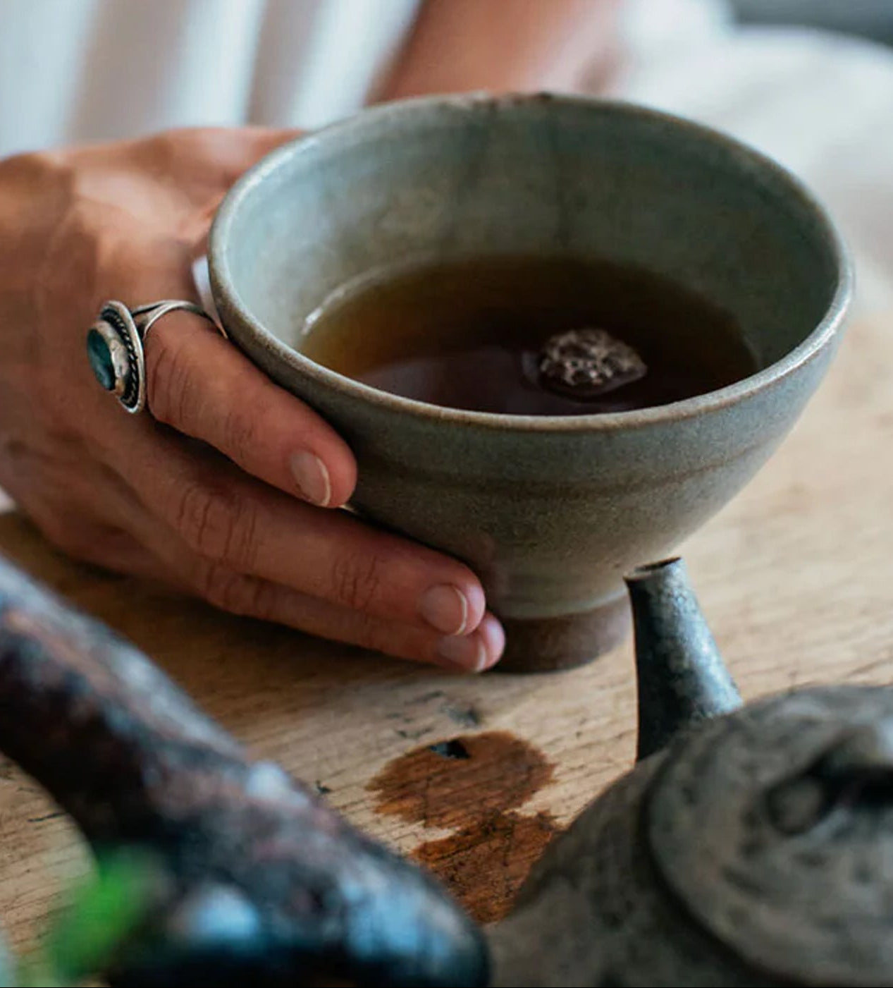 Person holding a ceramic teacup with tea on a wooden surface